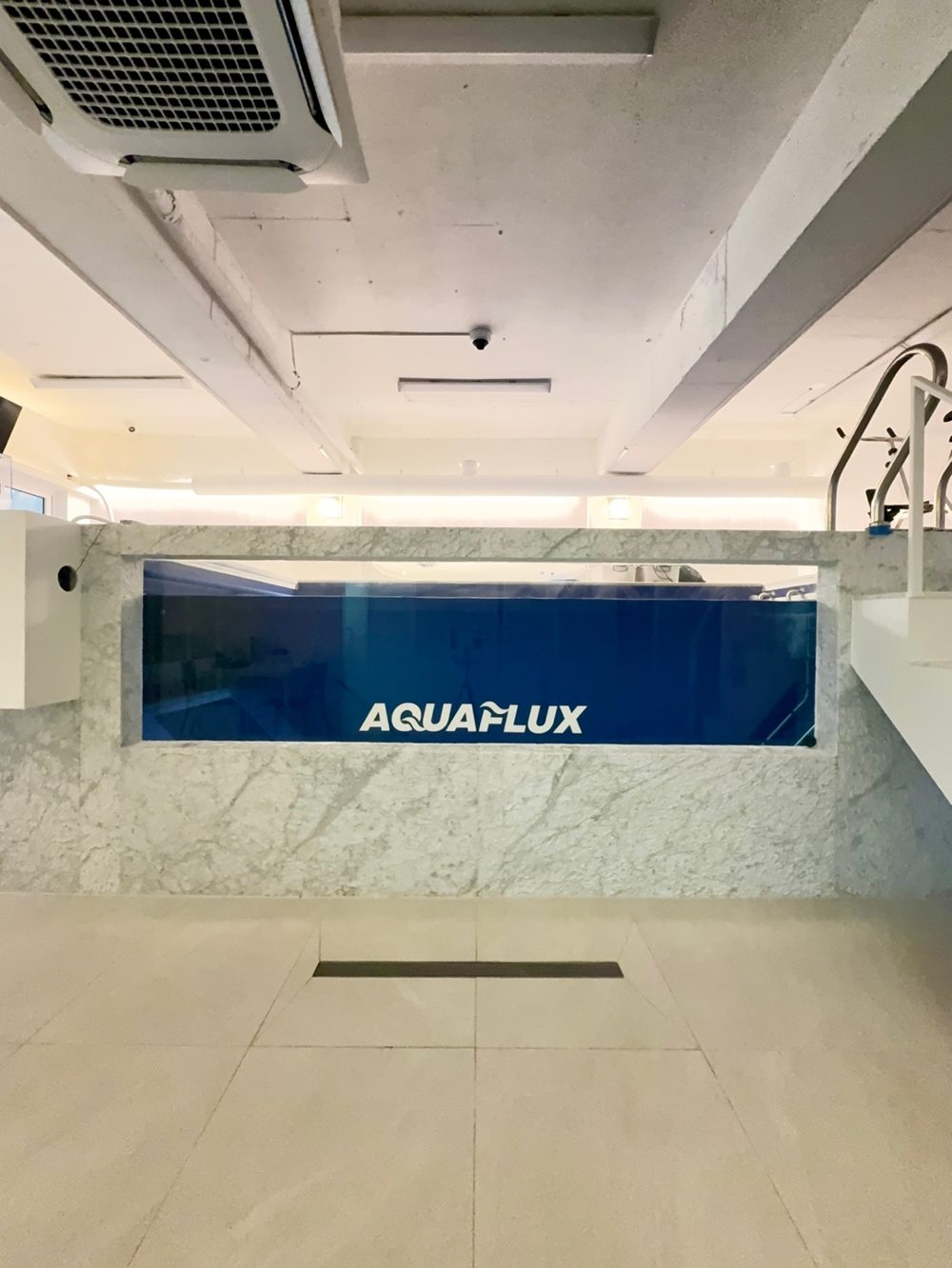 관측창 너머로 AQUAFLUX 로고가 보이는 수영장